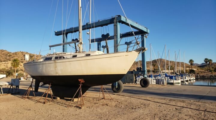 Velero de crucero de 35 pies en seco sobre picaderos en un varadero, con el travelift al fondo y la marina detrás
